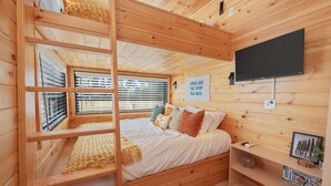 A cozy wooden cabin room with a bunk bed, a flat-screen TV, and a window with blinds.