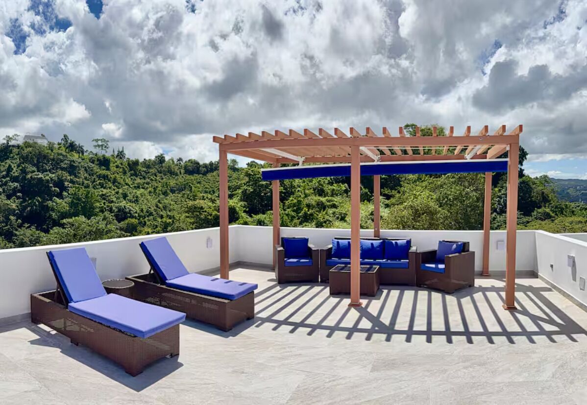 Une terrasse sur le toit, dotée de chaises longues et d’une pergola en bois, offrant une vue sur un paysage boisé.