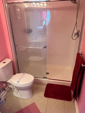 A bathroom with a toilet, a shower enclosure, and a red bath mat. - Less Stress Express ; A trip to your wants & Needs (osceola)