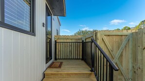 A wooden deck with a black railing, a wooden fence, and a clear blue sky.