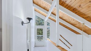 Ein Flur mit Holzboden, weißer Wand und einer Tür zu einem Balkon mit Blick auf Bäume.