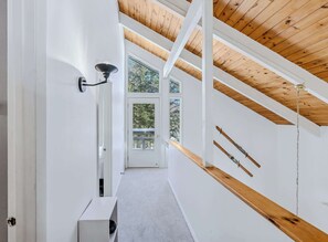 A hallway with a wooden ceiling, a white wall, and a door leading to a balcony with a view of trees. - Quechee Club Access: Pool, Golf + Fireplace (Quechee)