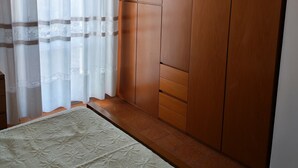 Une chambre à coucher avec un lit, une armoire en bois et des rideaux légers.