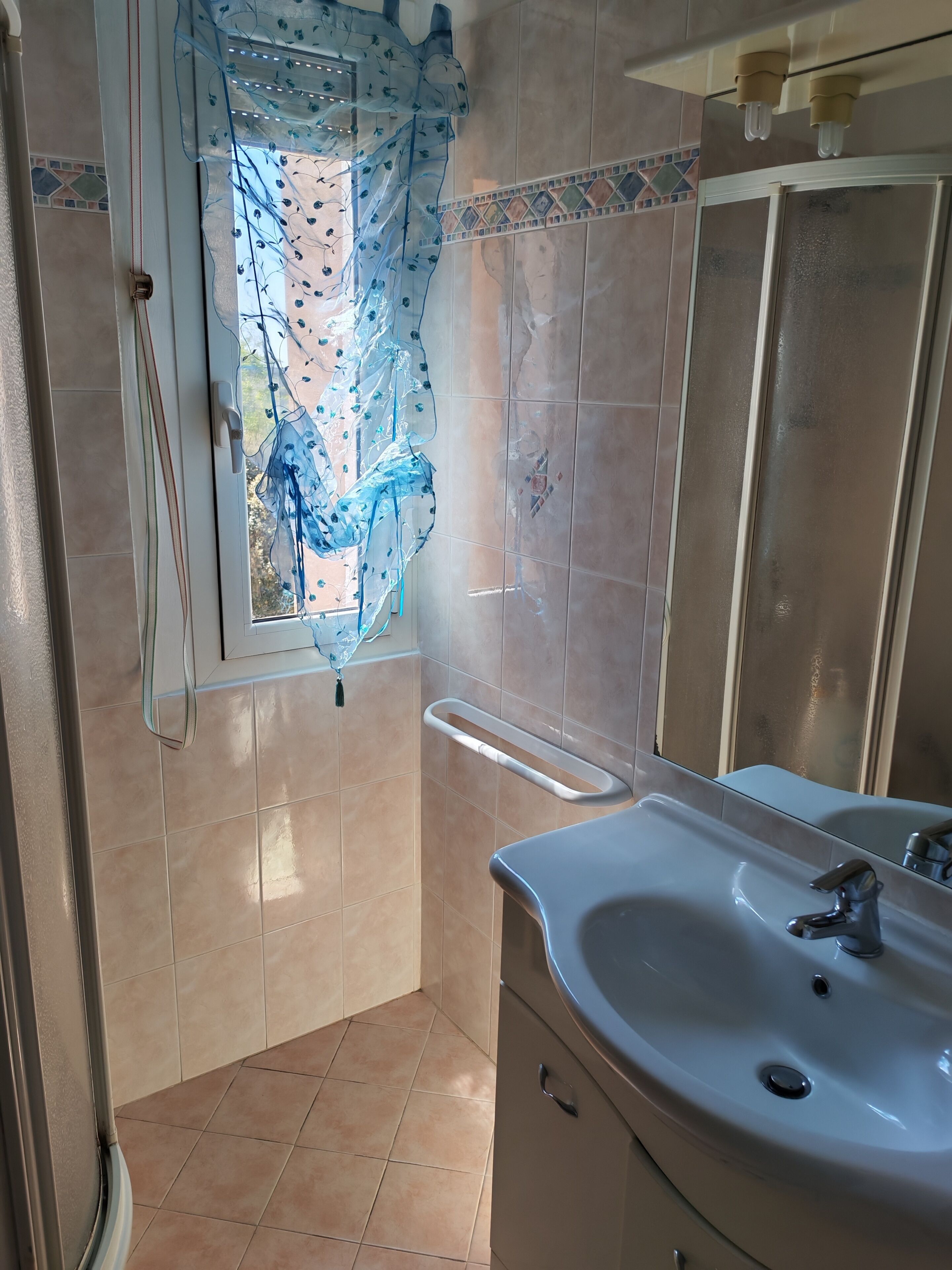 Une salle de bain avec un lavabo, un miroir et une fenêtre ornée d’un rideau bleu.
