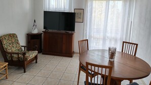 Un salon avec un téléviseur, des meubles en bois, une table à manger et un lustre.