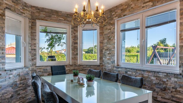 En matplats med ett glasbord, stenmurar och stora fönster med persienner.