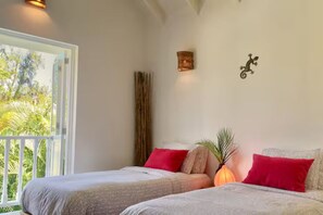 Une chambre avec deux lits, une fenêtre donnant sur un espace verdoyant, un luminaire fixé au mur et un petit objet décoratif.