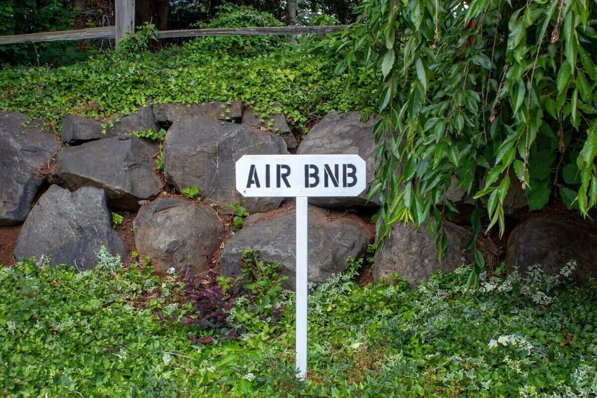 Skilt med teksten 'AIR BNB' i en have med sten og grønt.