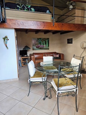A dining area with a glass table surrounded by metal chairs, a brown leather sofa, and a painting on the wall.