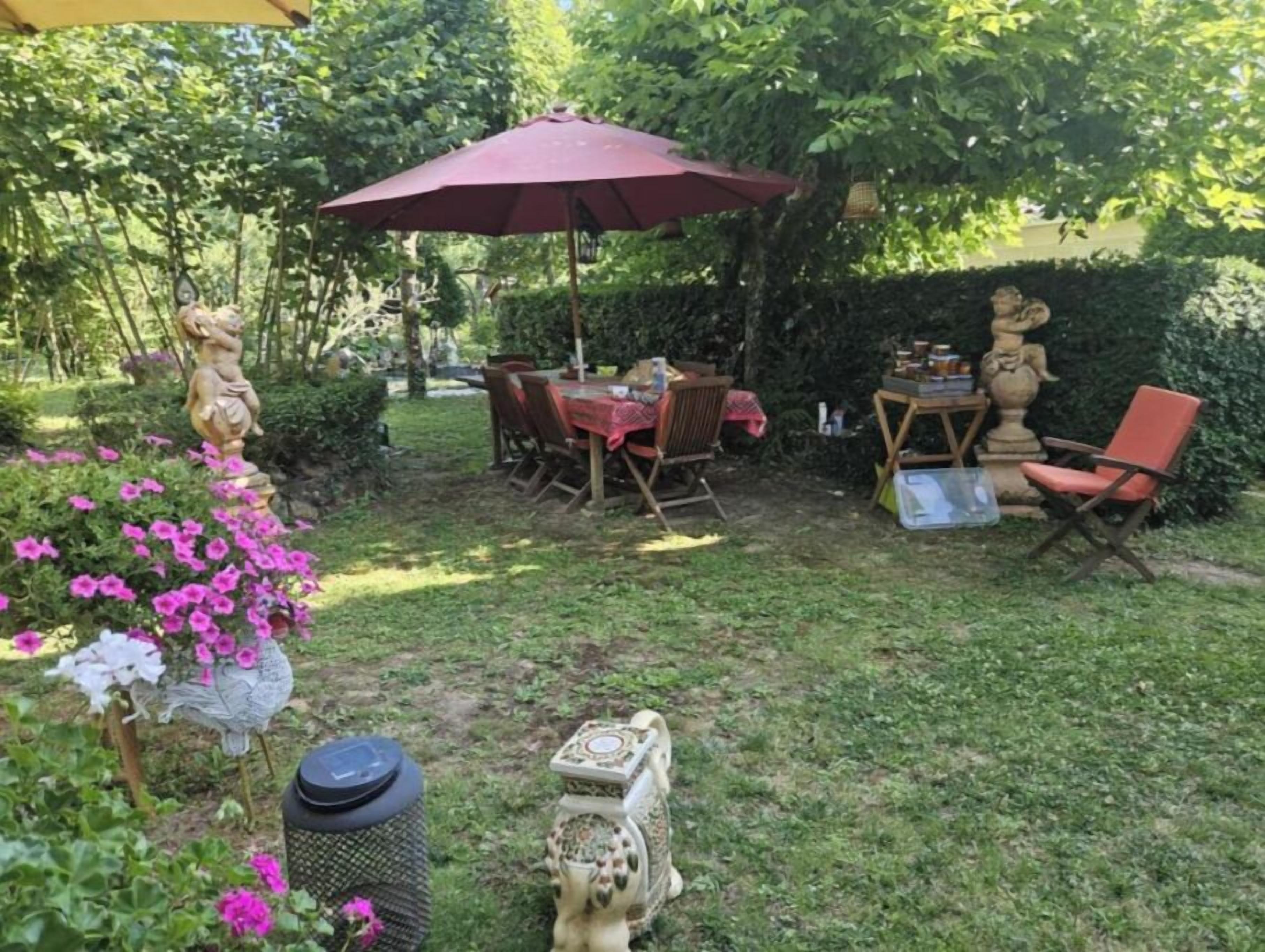 A garden patio with a table and chairs, a decorative statue, and a trash can.