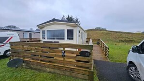 Una casa móvil con un ventanal grande y una terraza, rodeada de una valla de madera con el número 53.