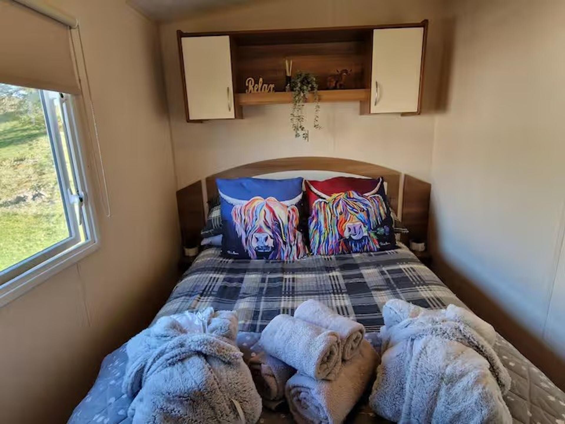 A bed with colorful lion-themed pillows, a plaid bedspread, and rolled towels on the floor.