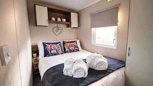 Un dormitorio con cama, almohadas, un adorno con forma de corazón, una ventana y un perchero para toallas.