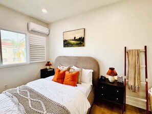 Una camera da letto con un letto, due comodini, un condizionatore d'aria, una finestra e un quadro appeso al muro.