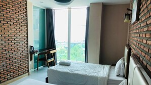 Ett hotellrum med två sängar, en tegelvägg som accent, ett stort fönster med gardiner och utsikt över grönområden utanför.