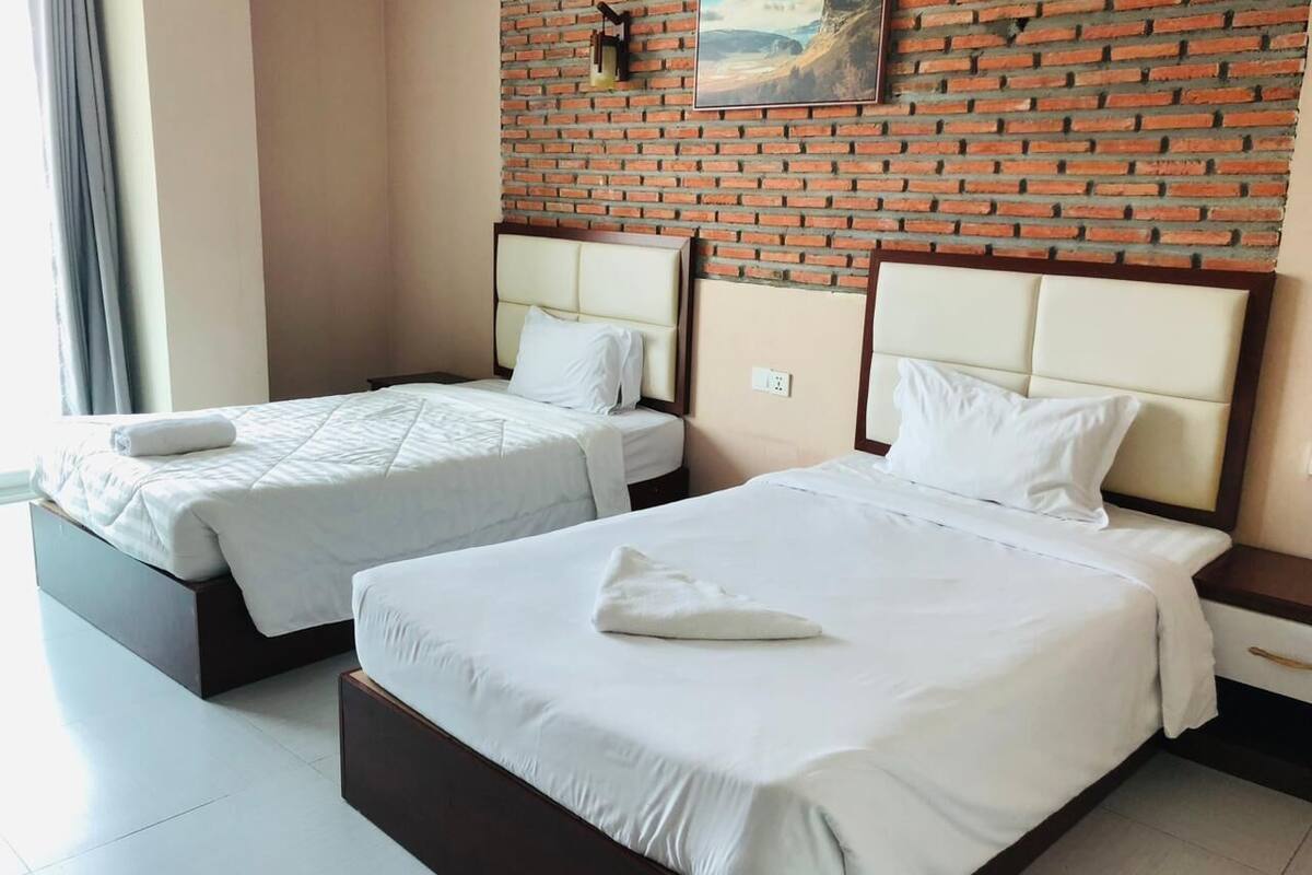 A hotel room with two beds, a brick wall, and a painting.