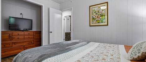 A bedroom with a bed, a dresser, a television, and a framed floral artwork on the wall.