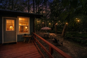 A cabin with a wooden deck, a dining area with outdoor furniture, and string lights.