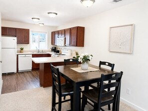 A modern kitchen with wooden cabinets, a central island, and a dining table with chairs.