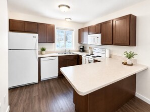A modern kitchen with wooden cabinets, a white refrigerator, a microwave, and a dishwasher.
