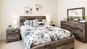 Quarto com estrutura de cama de madeira, mesa de cabeceira com abajur, cômoda e espelho.