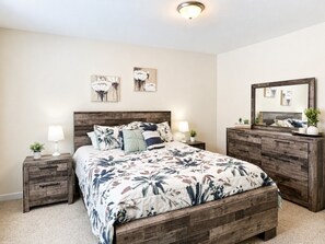 A bedroom with a wooden bed frame, a nightstand with a lamp, a dresser, and a mirror.
