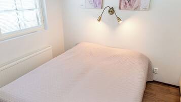A bedroom with a bed, a radiator, a window with blinds, and two wall-mounted paintings.