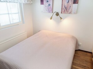 Un dormitorio con cama, un radiador, una ventana con persianas y dos cuadros colgados en la pared.