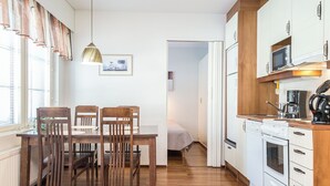 Une cuisine compacte avec des meubles en bois, un coin repas comprenant une table et des chaises, et un lit visible dans la pièce adjacente.