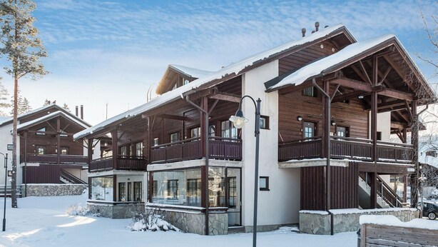 Un chalet en bois à plusieurs étages, doté de balcons, de grandes fenêtres et de fondations en pierre.