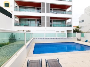 Ein modernes Gebäude mit Schwimmbecken, zwei Balkonen und einer überdachten Terrasse.