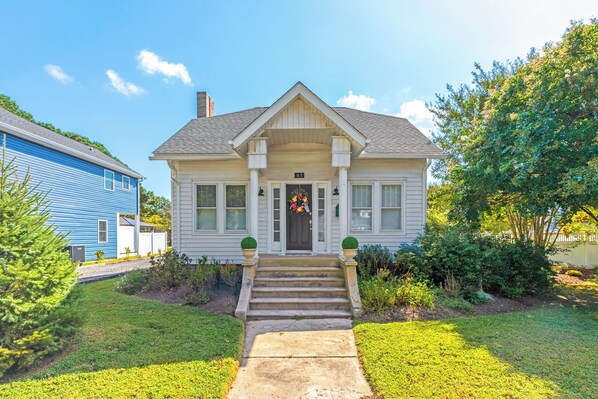 A two-story house with a front porch, a number '61' sign above the door, and a flower wreath.