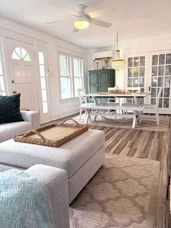 A spacious living room with a large white sofa, a dining area with a white table and chairs, and a ceiling fan.