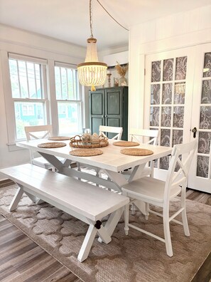 A dining area with a white table, benches, and chairs. There is a chandelier hanging above the table.