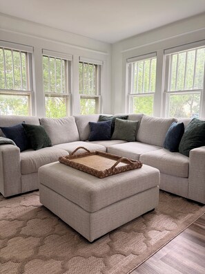 A living room with a sectional sofa, a woven tray, and a patterned rug.