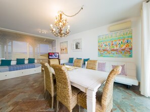 A spacious living area with a large dining table, wicker chairs, and a television. - Mar a Vista T1 by YHA (Cabanas de Tavira)