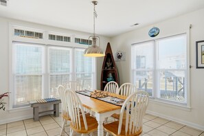 A dining area with a wooden table, white chairs, and a hanging pendant light. - 4-bedroom house across from Ocean and Ocean Crest pierwith water view (Oak Island)