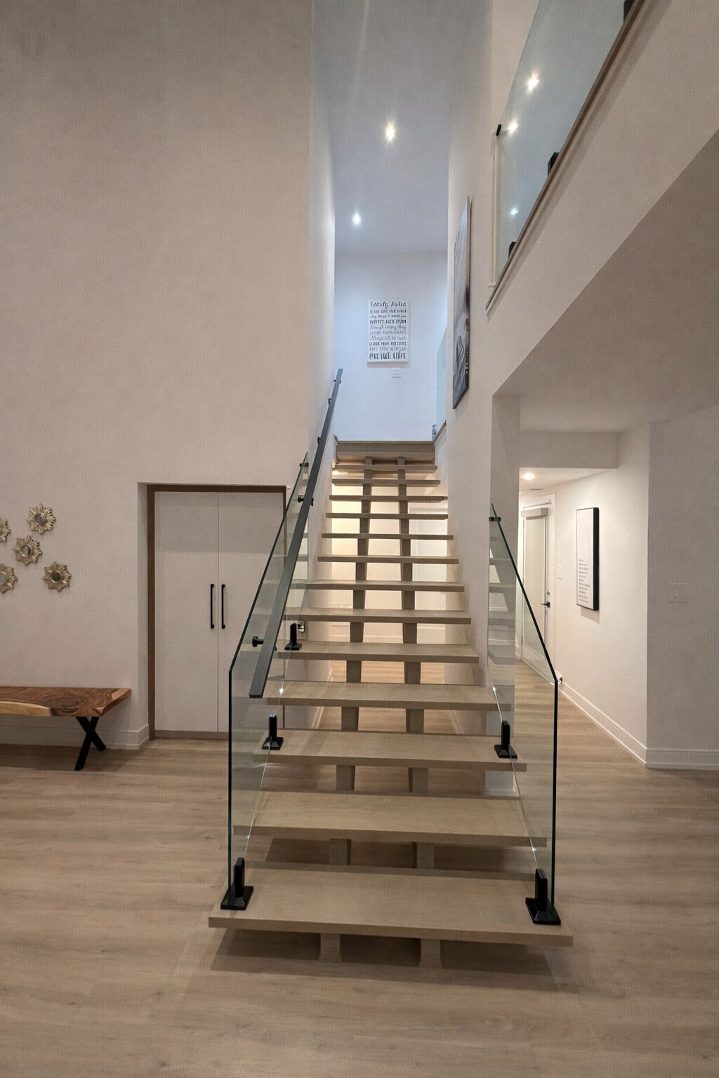Una escalera moderna con barandillas de vidrio y peldaños de madera, que conduce a un piso superior.