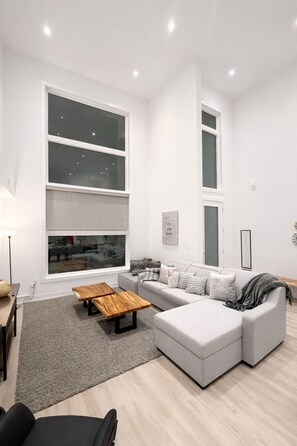 Ein modernes Wohnzimmer mit einem grauen Ecksofa, einem Holztisch und einem grauen Teppich.