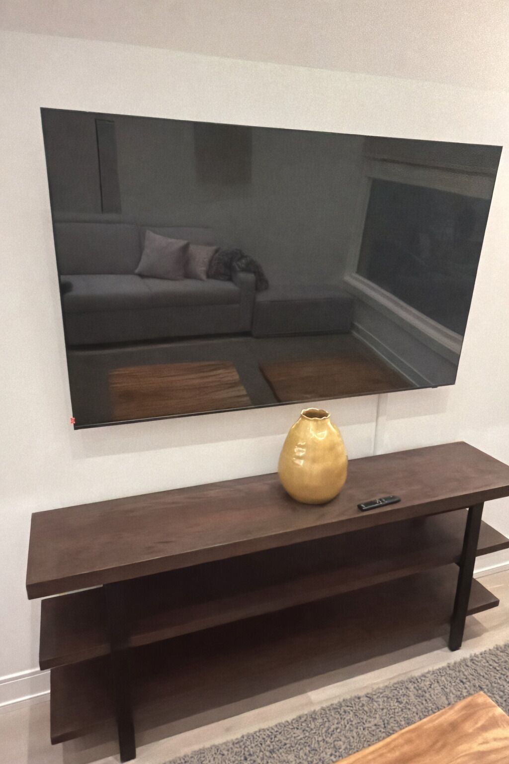 Un salon moderne avec un grand téléviseur à écran plat fixé au mur, une console en bois foncé placée en dessous et un vase décoratif sur la table.