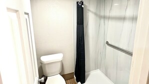 Egy fürdőszoba, amelyben található egy WC, egy üvegajtós zuhanyzó és egy fehér fürdőkád.