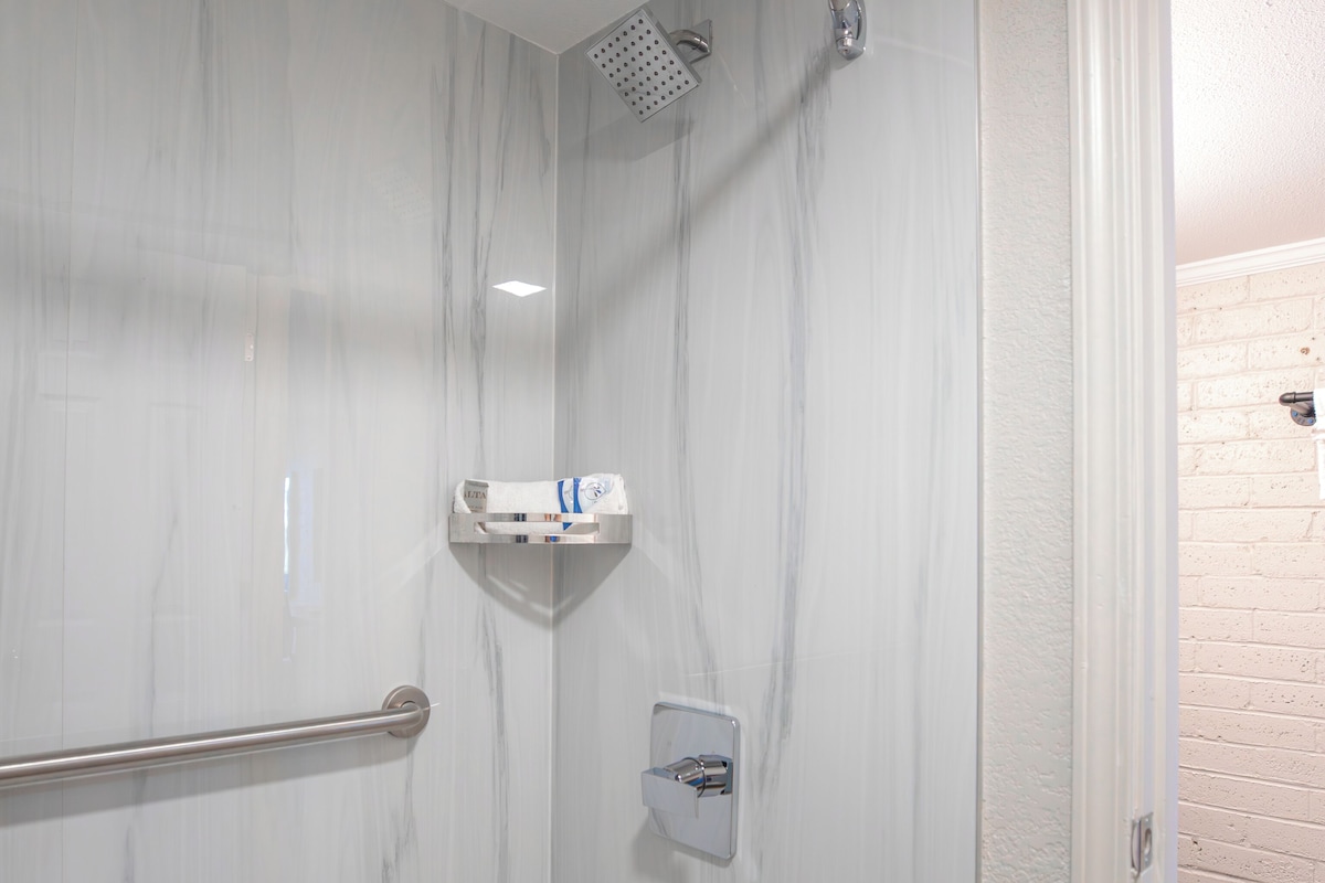 A modern bathroom with a shower, marble walls, and a wooden floor.