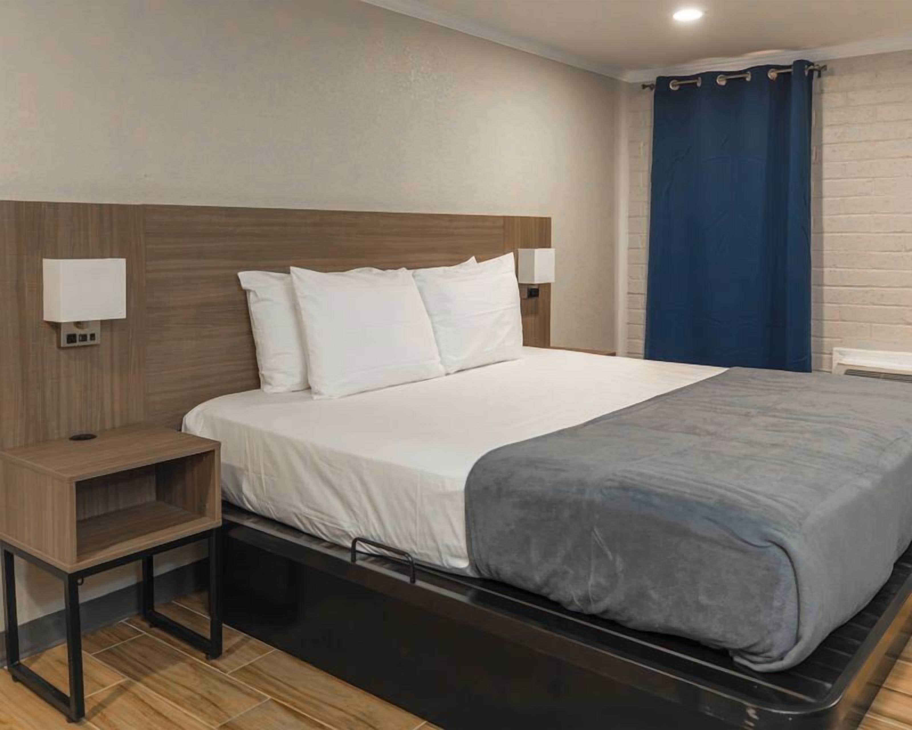 A hotel room with a bed, bedside tables, a nightstand, and a window with curtains.