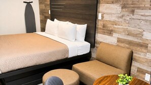 Habitación de hotel moderna con cama, sofá, sillón, mesita con planta y un elemento decorativo en la pared.