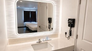 Un baño moderno con un espejo grande, un lavabo, un secador de pelo y un teléfono.