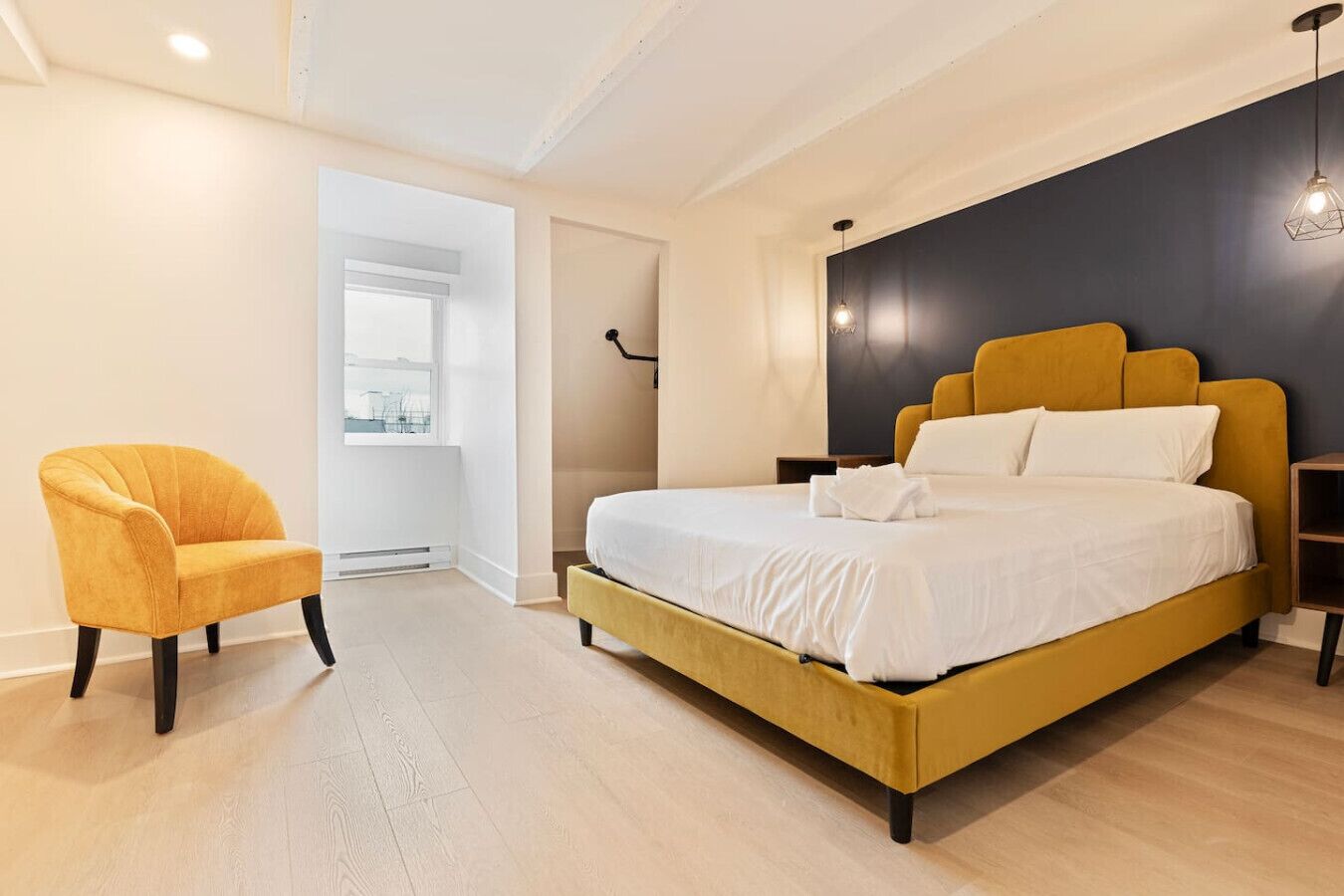 A modern bedroom with a yellow bed, a yellow armchair, and a large window.