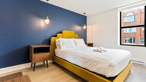 A modern hotel room with a yellow bed, white bedding, and a view of a brick building through a window. - Elegant Historic Suite | Two Floors of Luxury (Montreal)