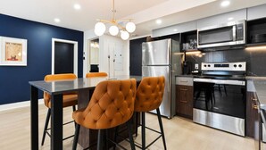 A modern kitchen with stainless steel appliances, a dining area with two orange chairs, and a ceiling light fixture. - Elegant Historic Suite | Two Floors of Luxury (Montreal)