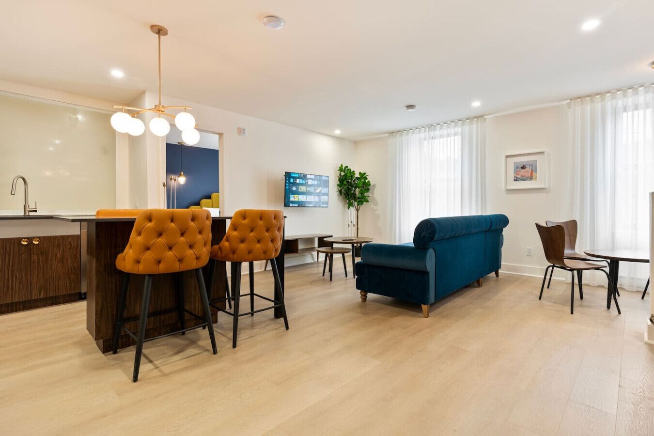 Un salon moderne avec un canapé bleu, un coin repas doté d’un bar, et une cuisine équipée d’un évier et de tabourets.