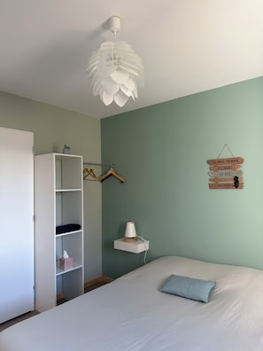 Een slaapkamer met een bed, een kledingkast, een ophangrek, een nachtkastje met een lamp en een decoratie aan de muur.